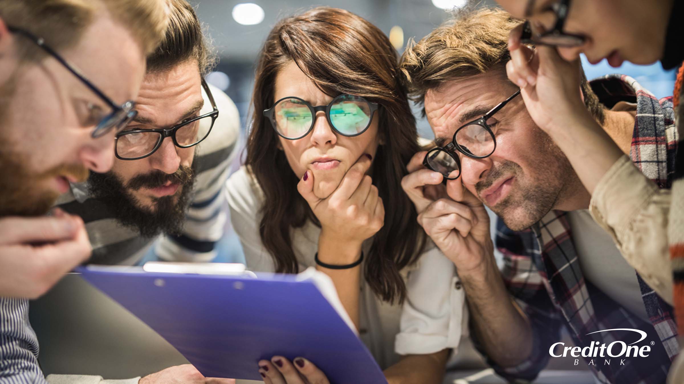 Several people gather around a clipboard and thoughtfully peer at the page as if trying to figure out how to read a credit report.